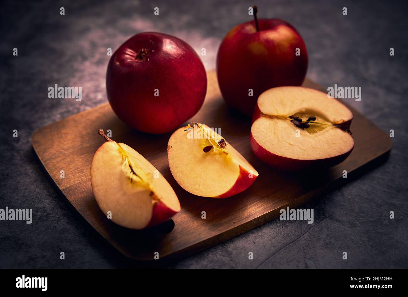 Apples board. Apples are on a cutting board and one apple is cut into a several pieces and the whole composition on a dark background Stock Photo