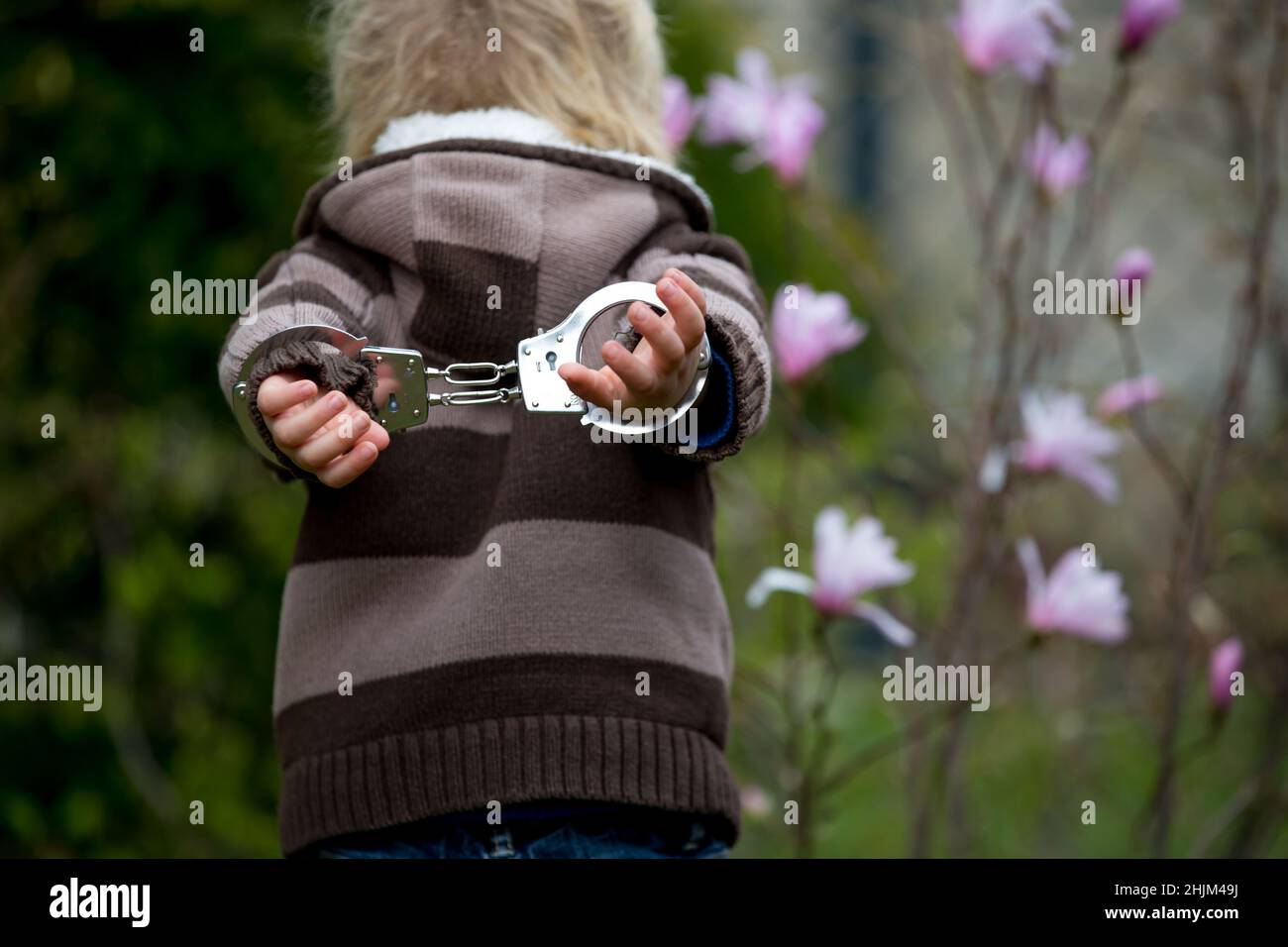 Child, boy in handcuffs, standing backwards in garden, waiting Stock Photo