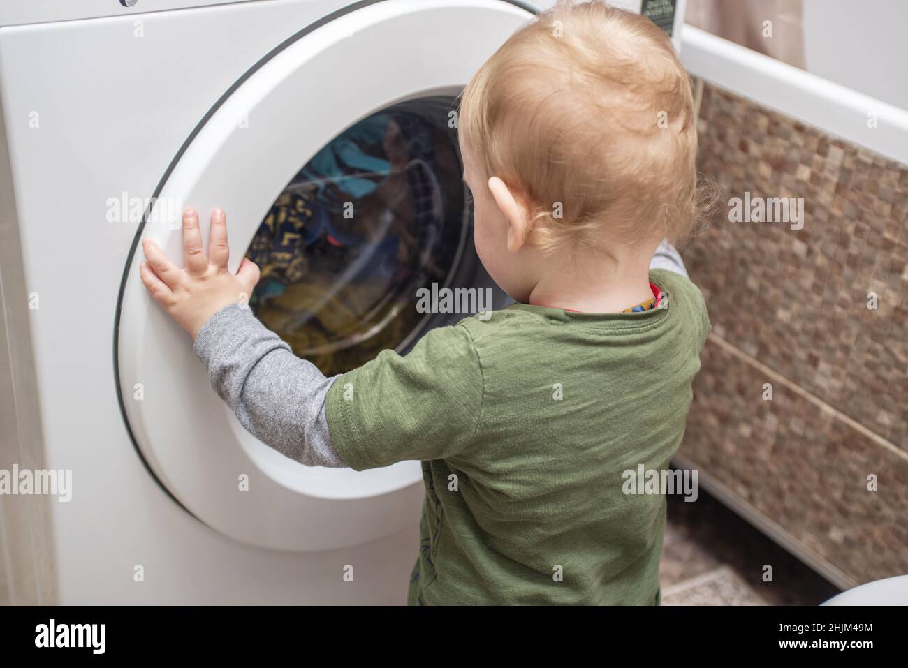 Child boy is looking into the washing machine. Baby boy interested in