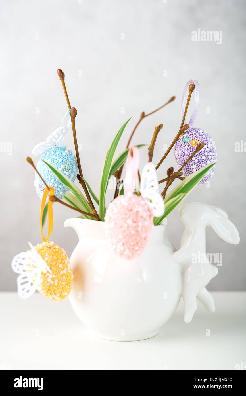 Home interior with easter decor. Vase with willow tree branches with Easter eggs and bunny on white table and background with copy space Stock Photo