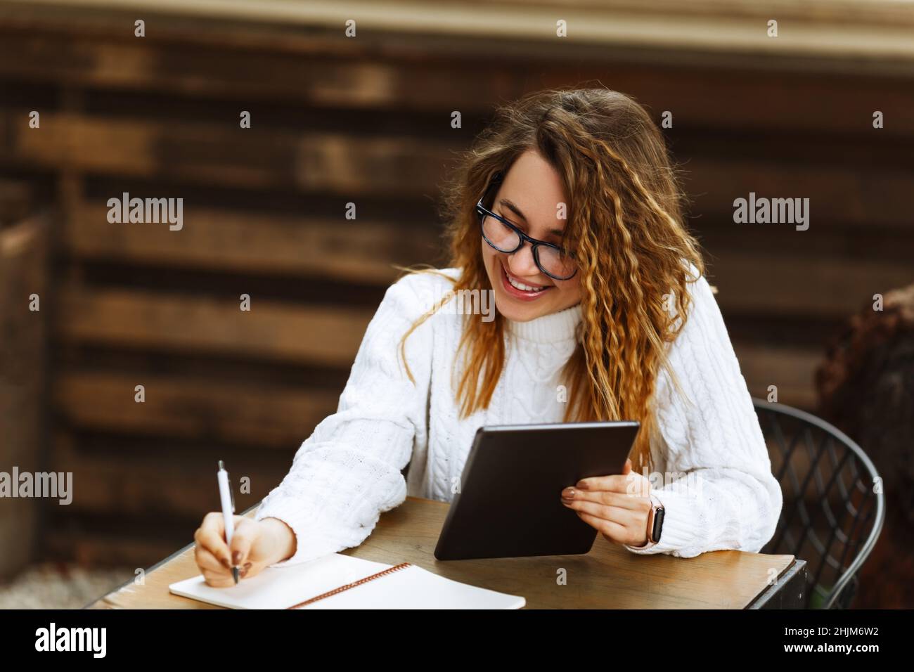 Young female student in glasses sitting at the table, using tablet when studying or working at cafe,using computer. Freelance business woman or student, blogging, studying, shopping, making notes. Stock Photo