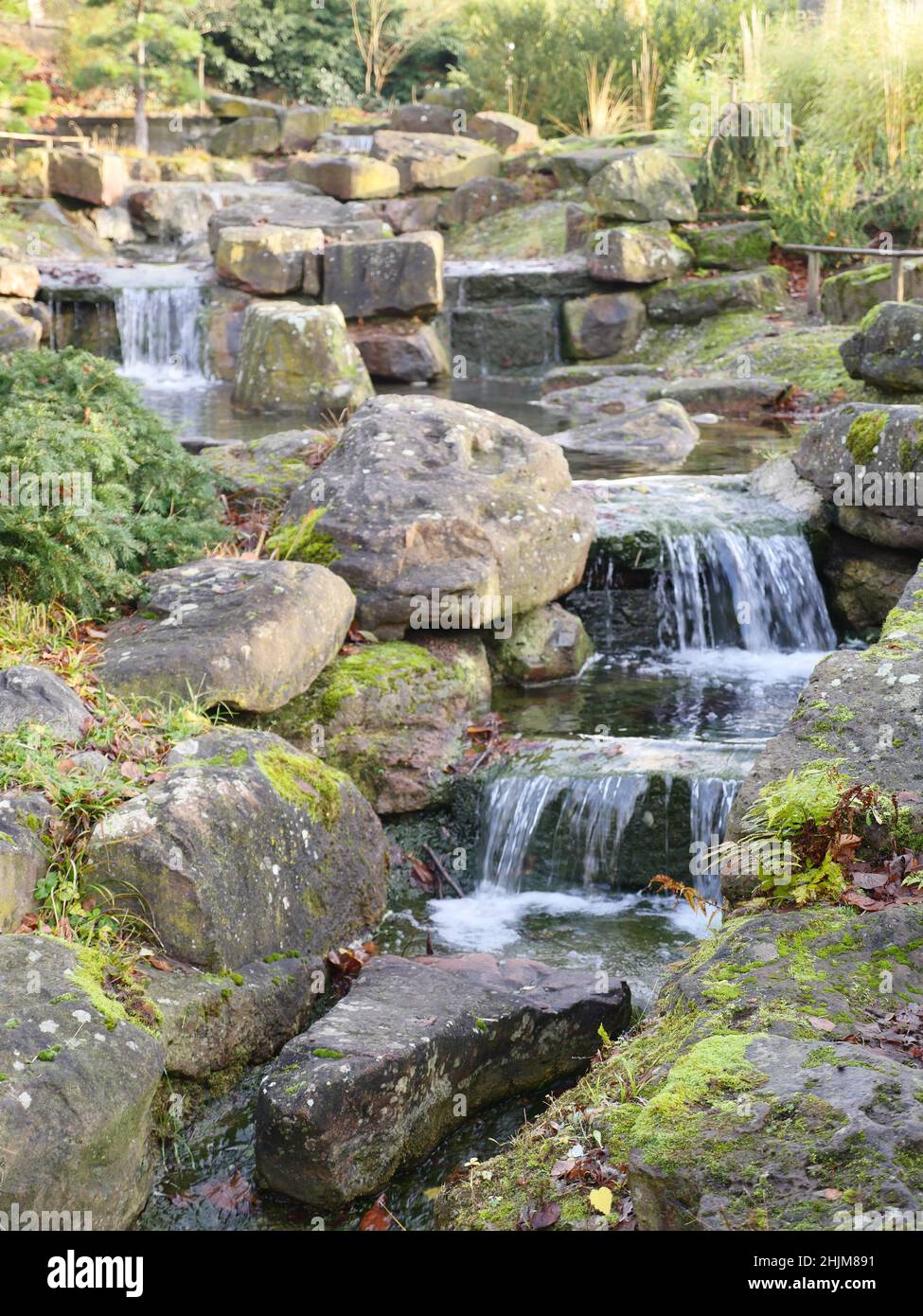 Small creek flows through a rocky environment, blurred background. The stones are partly overgrown with moss Stock Photo