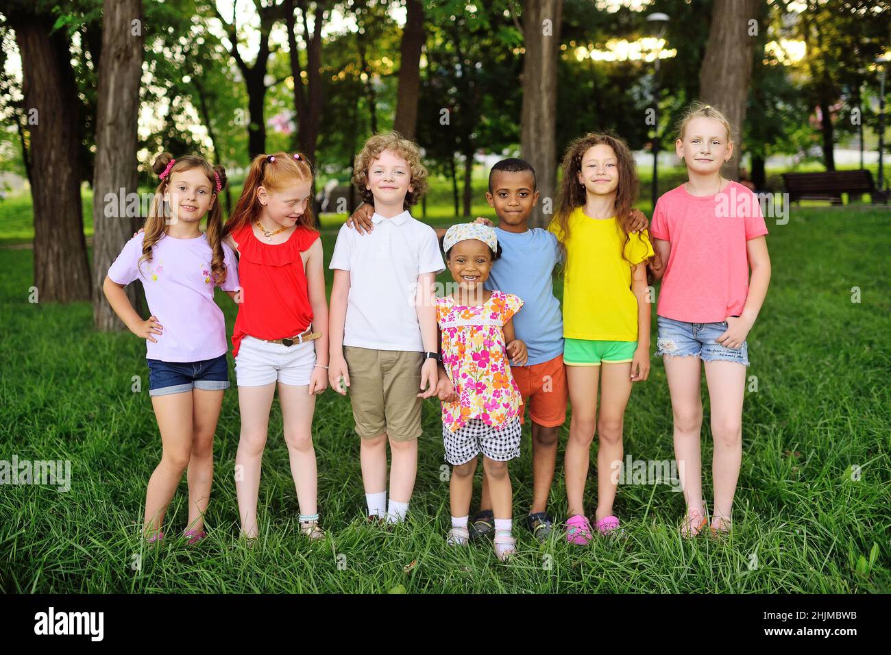 group of preschoolers of different races hug and smile against the background of greenery and a park. Children Protection Day. Stock Photo