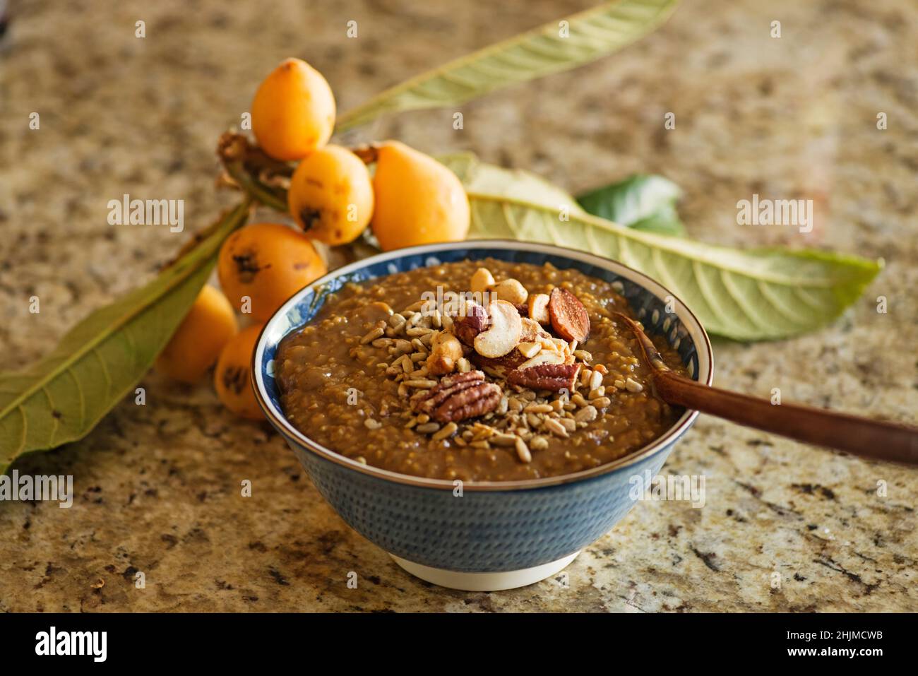a bowl of steel cut oatmeal with molasses topped with nuts with loquat behind it Stock Photo