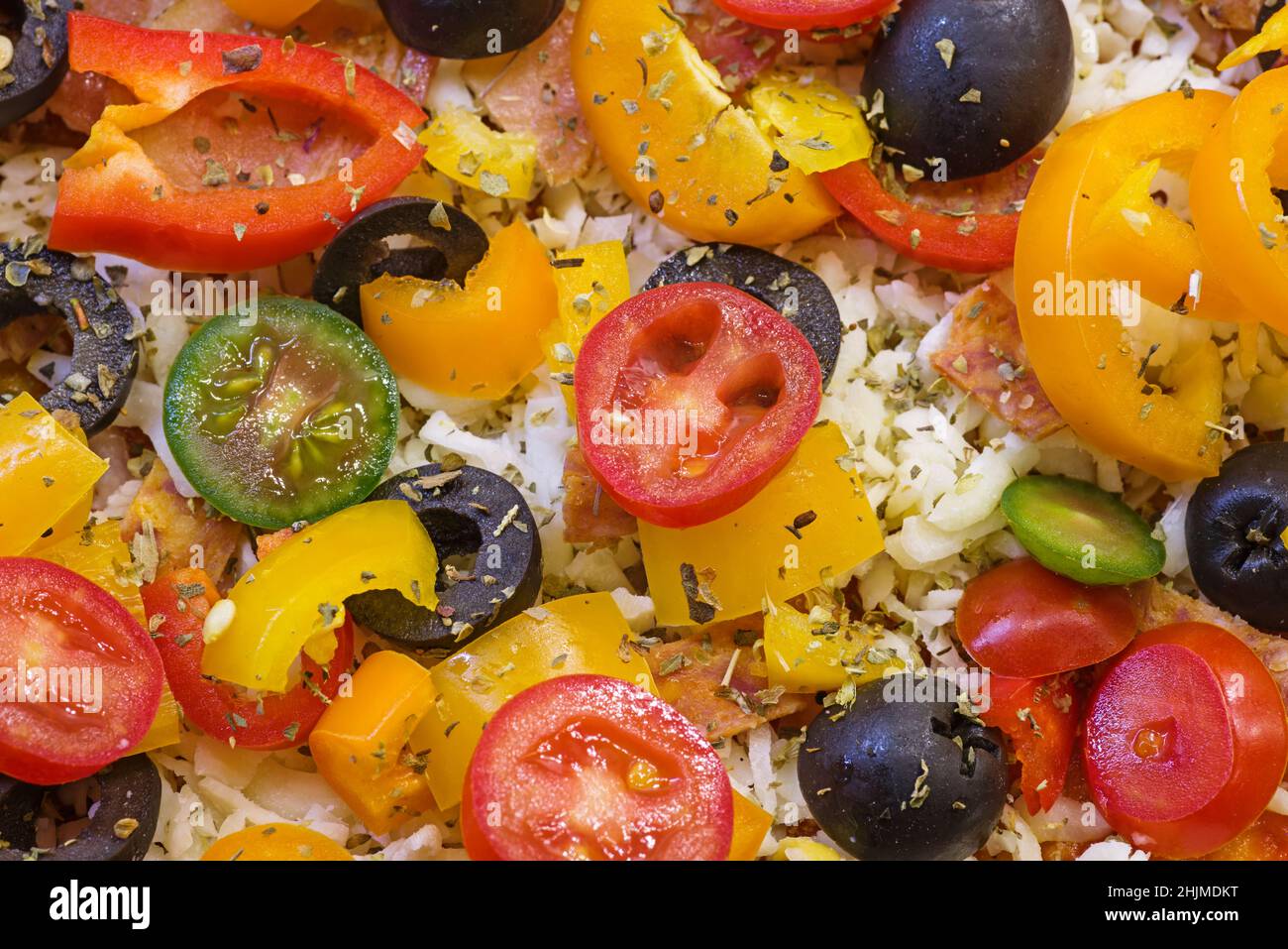 detail of an unbaked homemade pizza top with peppers tomato olives cheese and herbs ready to bake Stock Photo