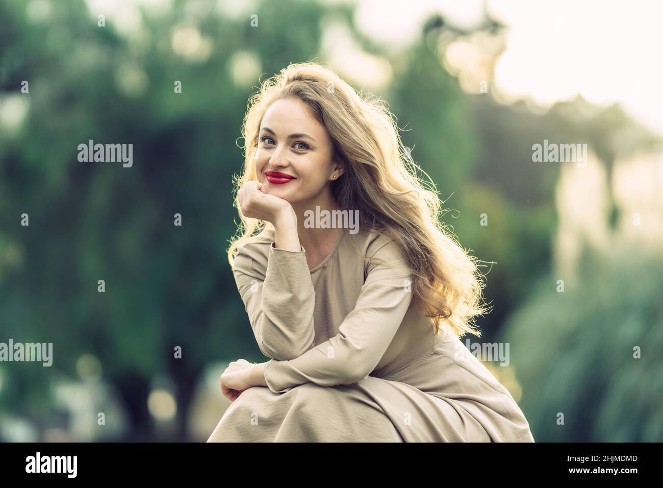 portrait of woman with long blonde hair squatting in a park at sunset Stock Photo