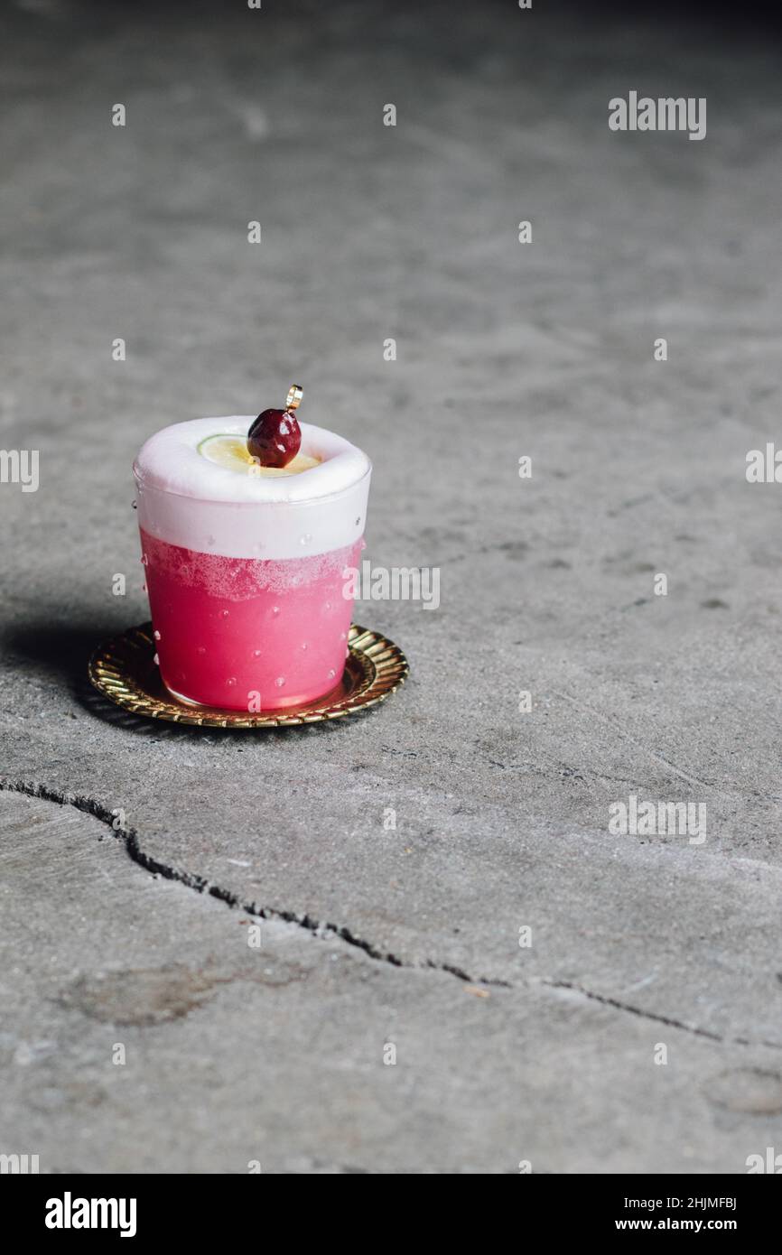 pink cocktail with white egg white foam and lime wheel, cherry on top garnish Stock Photo