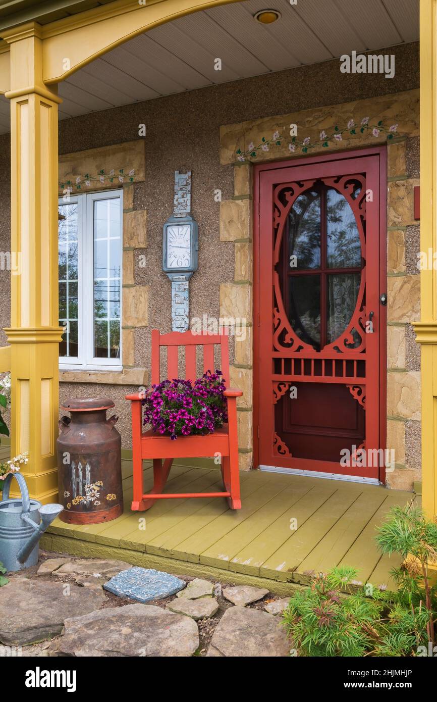 Flagstone patio and old house facade with veranda and Petunia x hybrida 'Purple Wave' flowers in planter on top of rocking chair in summer. Stock Photo