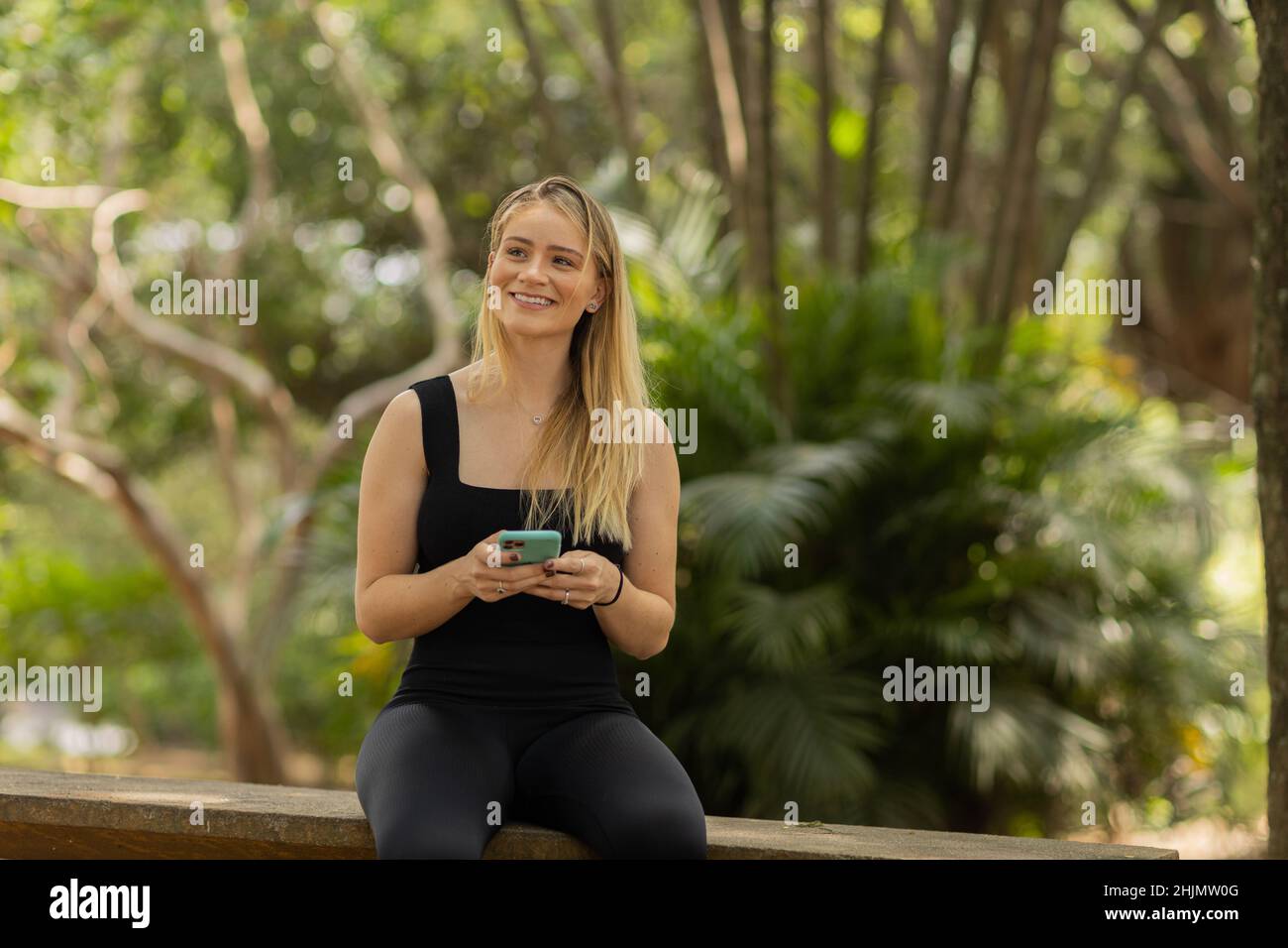 Young woman using a smartphone at day time with a green park in the background. High quality photo. Mobile phone, technology, urban concept. High qual Stock Photo