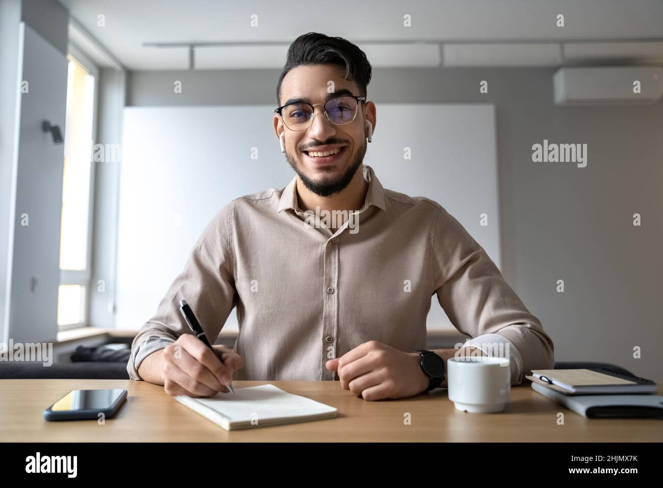 Smiling hindu man sitting at table holding pen for notes looking at camera Stock Photo