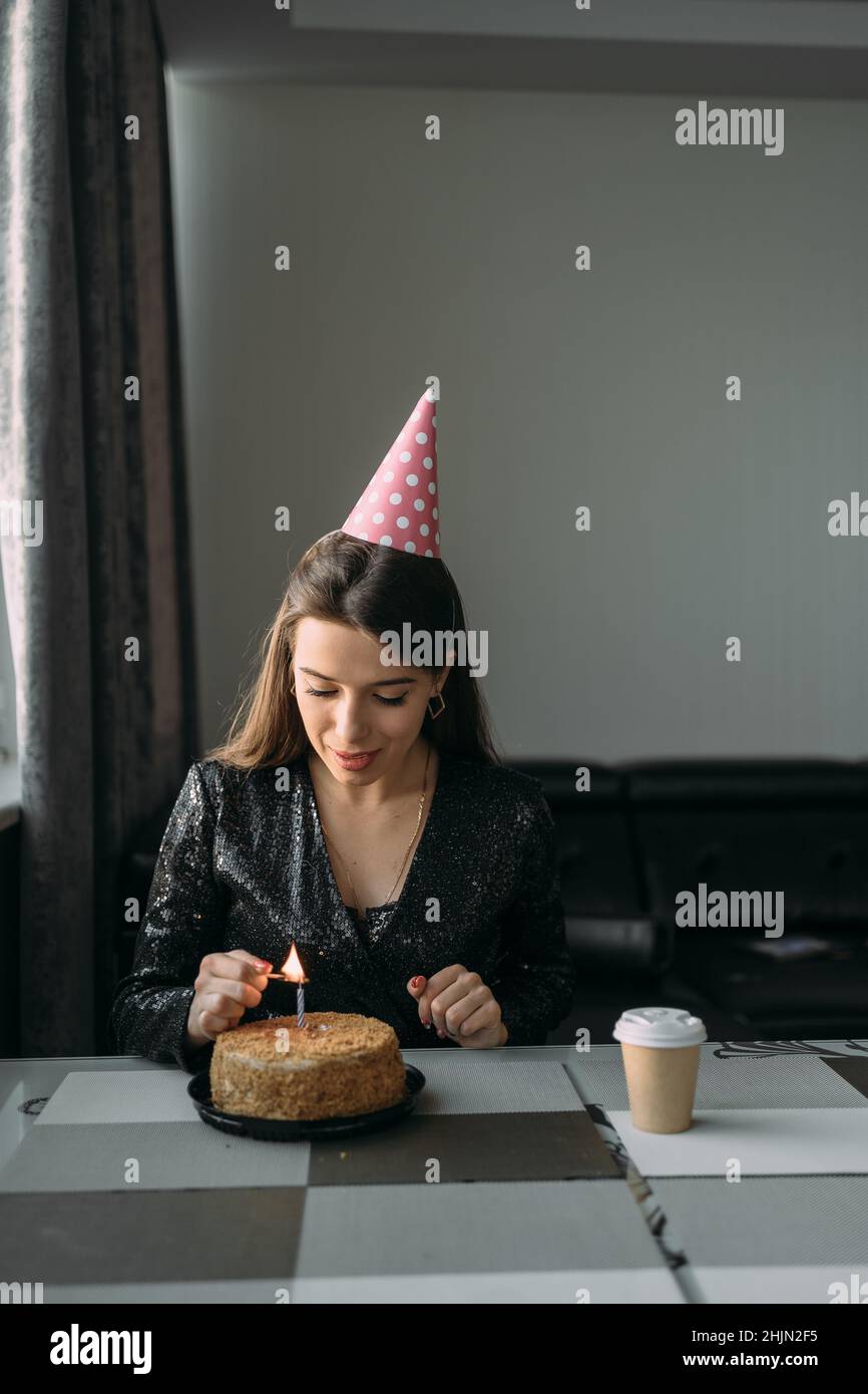 Caucasian girl lighting candle on cake, birthday at home, lonely woman celebrating anniversary with cake, introvert quarantine social distance Stock Photo