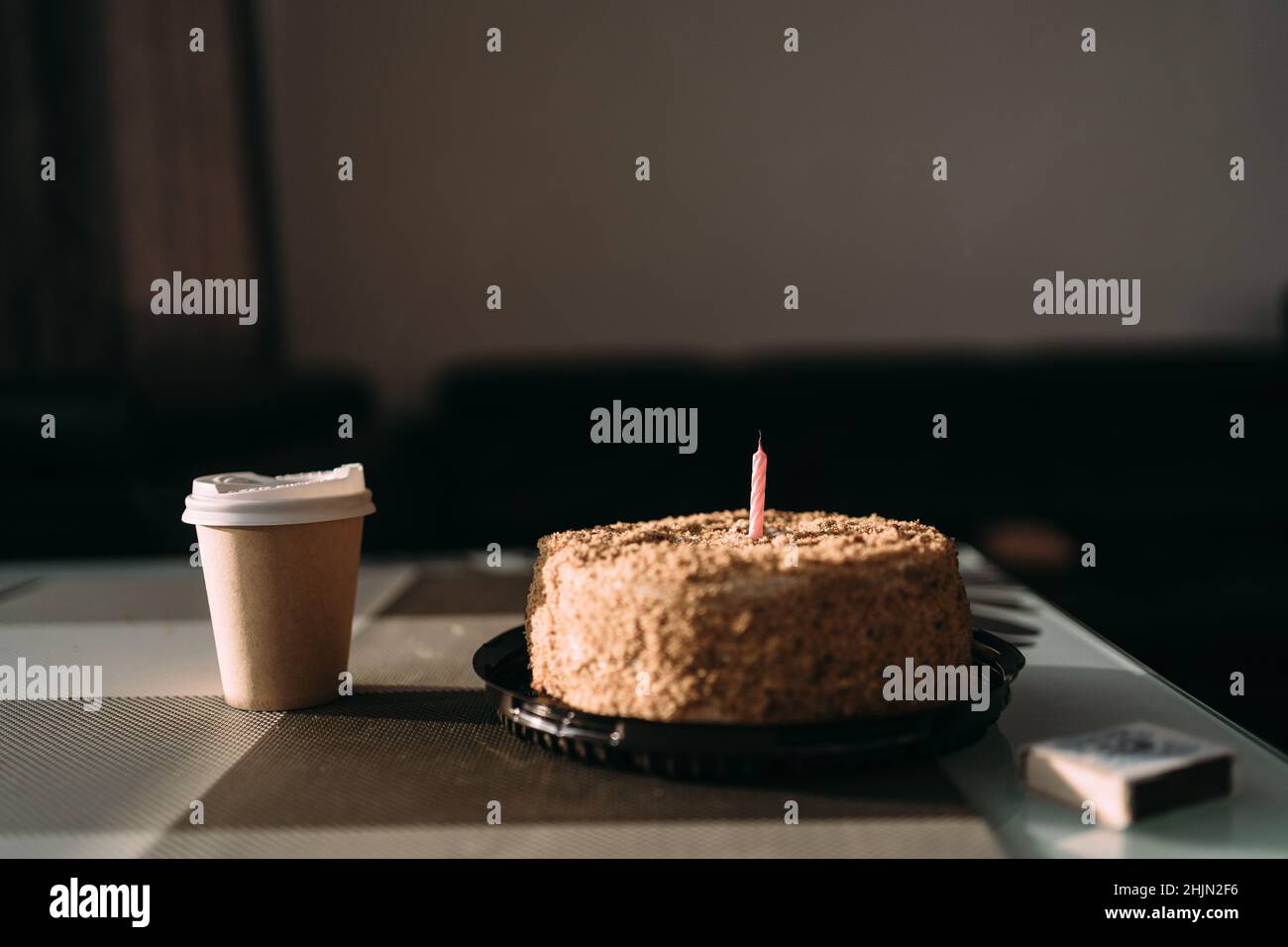 cake with one candle and a paper cup with coffee in a cafe. Breakfast Americano in a glass and a festive dessert. Birthday cake napoleon. Cafe menu Stock Photo