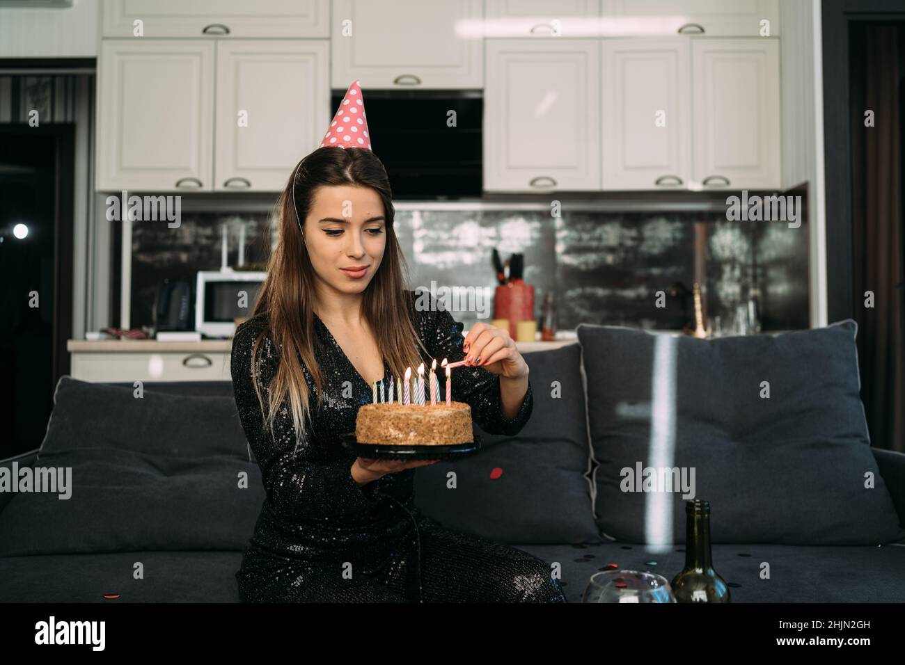 Smiling young woman lighting candles on cake, birthday party at home, sweet dessert with candles, european girl celebrating 25th birthday Stock Photo