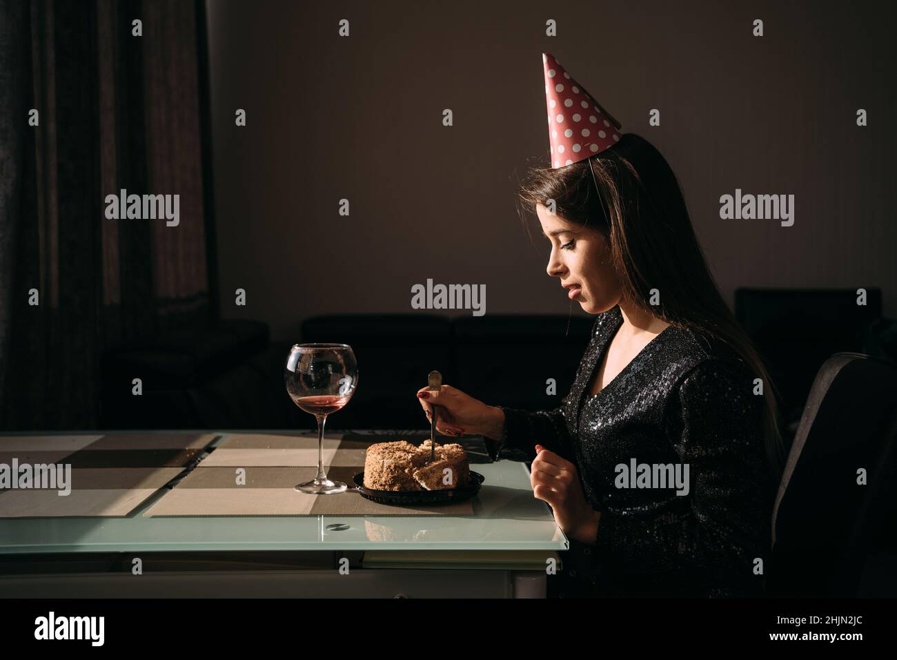 Caucasian young woman eating cake at table, female birthday party at home, holiday alone, celebrating anniversary with cake and wine, sweet dessert Stock Photo