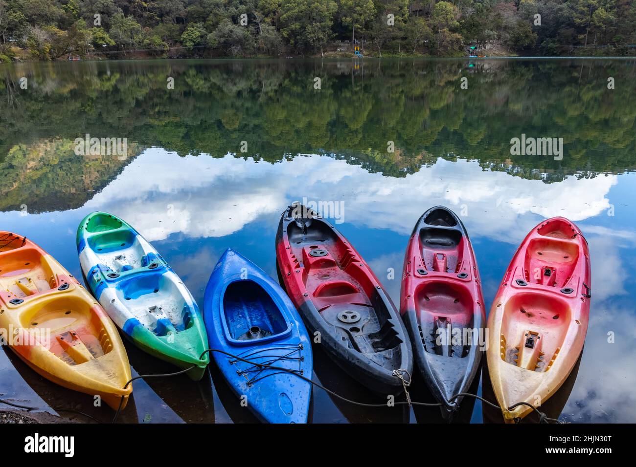 Colorful boats on the shore of a lake with the reflection of sky and hills Stock Photo