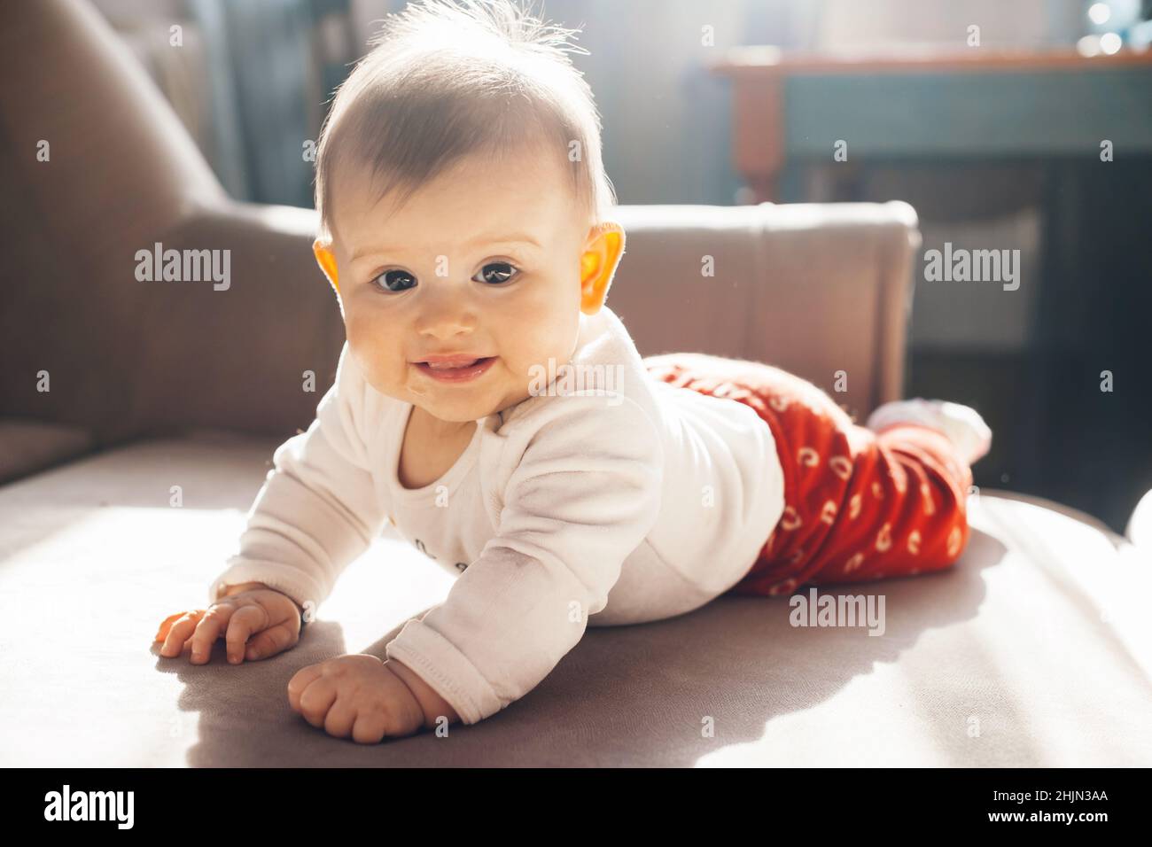 Baby girl lying on her belly on bed looking at camera and smiling. Baby care. Beauty face. Body care. Stock Photo