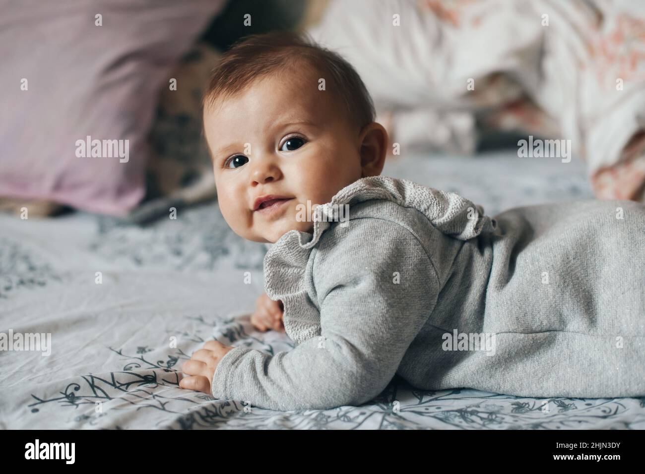 Caucasian baby girl wearing bodysuit crawling on bed while looking at camera. Beautiful closeup portrait. Stock Photo