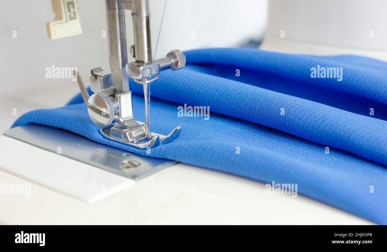Sewing machine foot with needle and blue fabric. sewing process. concept of making clothes .Empty space for text Stock Photo