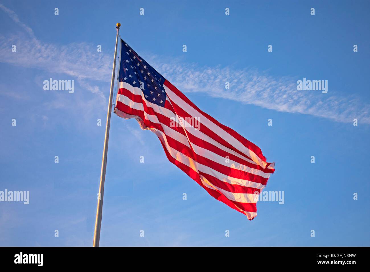 Single, large, isolated US flag flying high on a flagpole against a clear blue sky Stock Photo