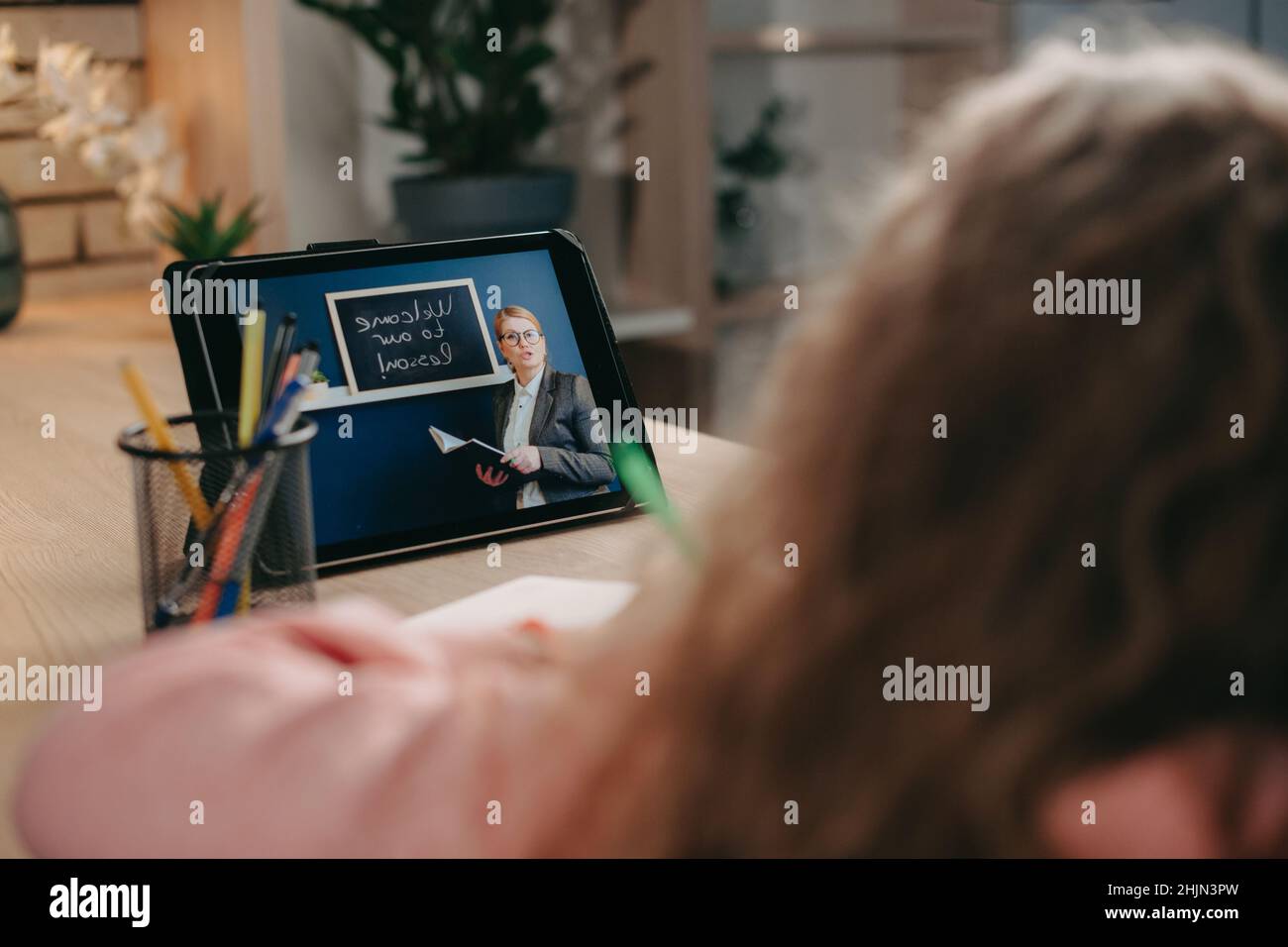 Back view of a schoolgirl kid talking with teacher tutor in virtual classroom using digital tablet. Writing test maths. Modern online education Stock Photo