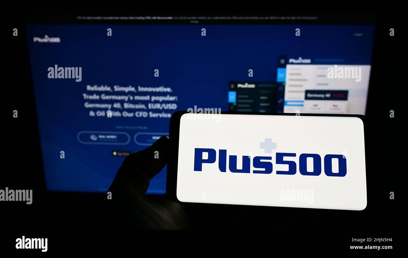Person holding smartphone with logo of CFD fintech company Plus500 Ltd. on  screen in front of website. Focus on phone display Stock Photo - Alamy