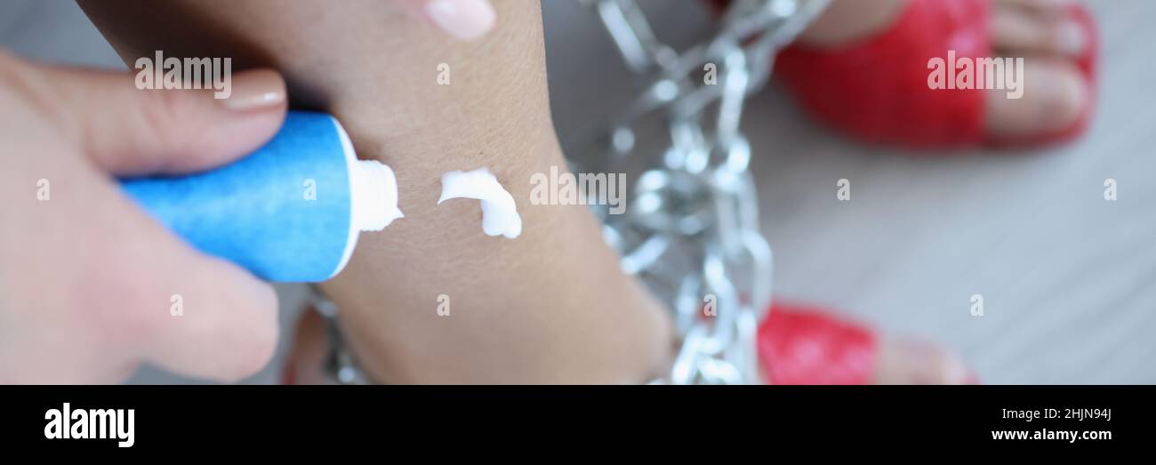 Woman applies cream to legs tied with chain closeup Stock Photo