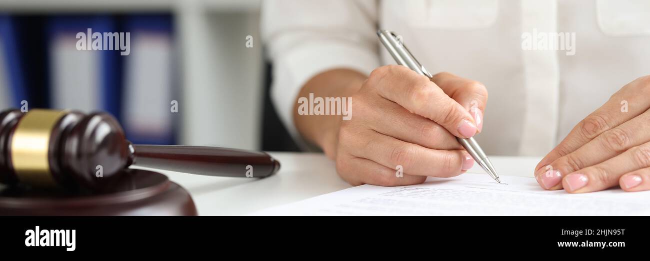 Female hand signs agreement near wooden judge gavel Stock Photo