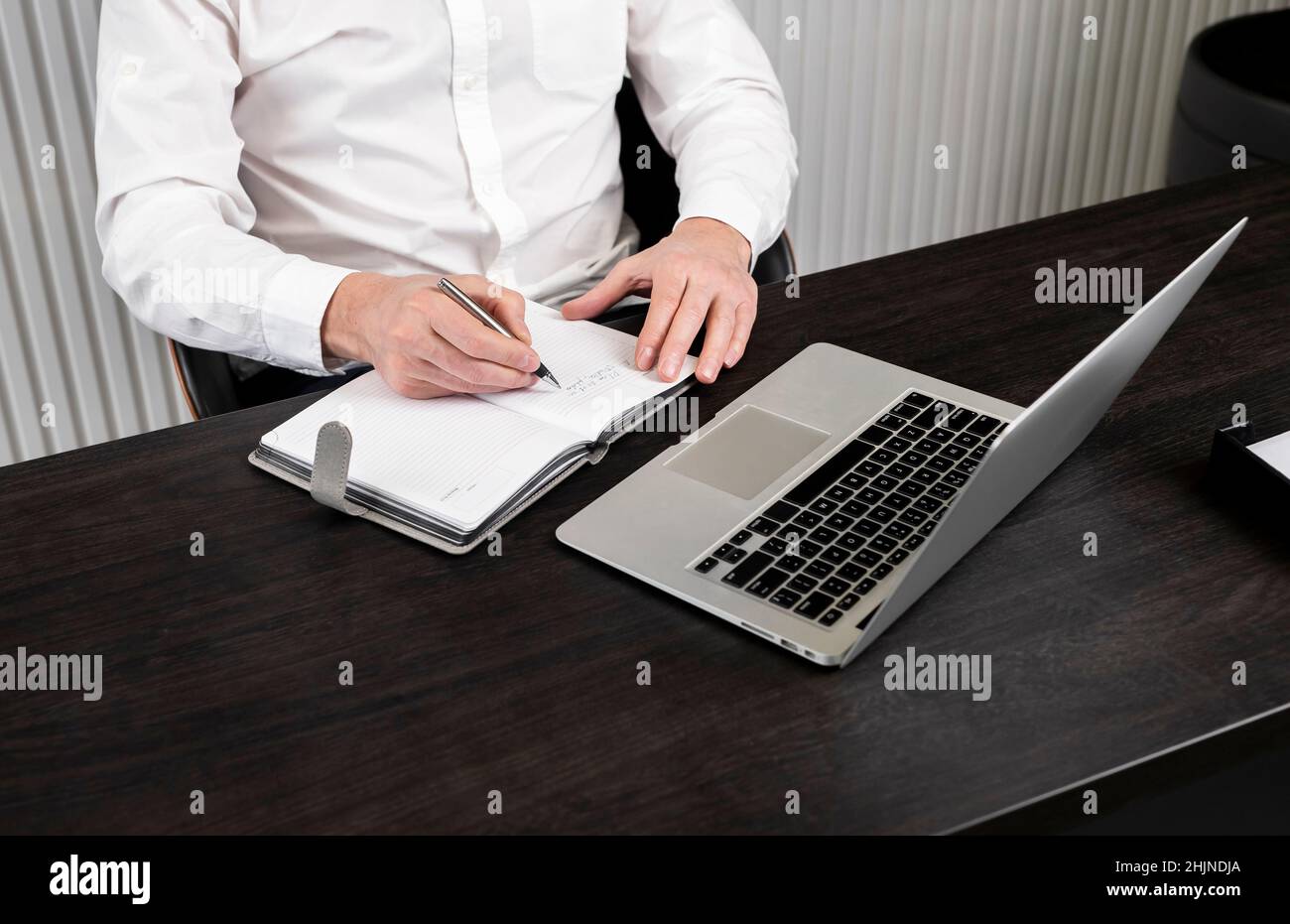 Man taking notes in planner. Businessman sitting at desk and working or studying on laptop. Online education or using computer technology in work concept. High quality photo Stock Photo