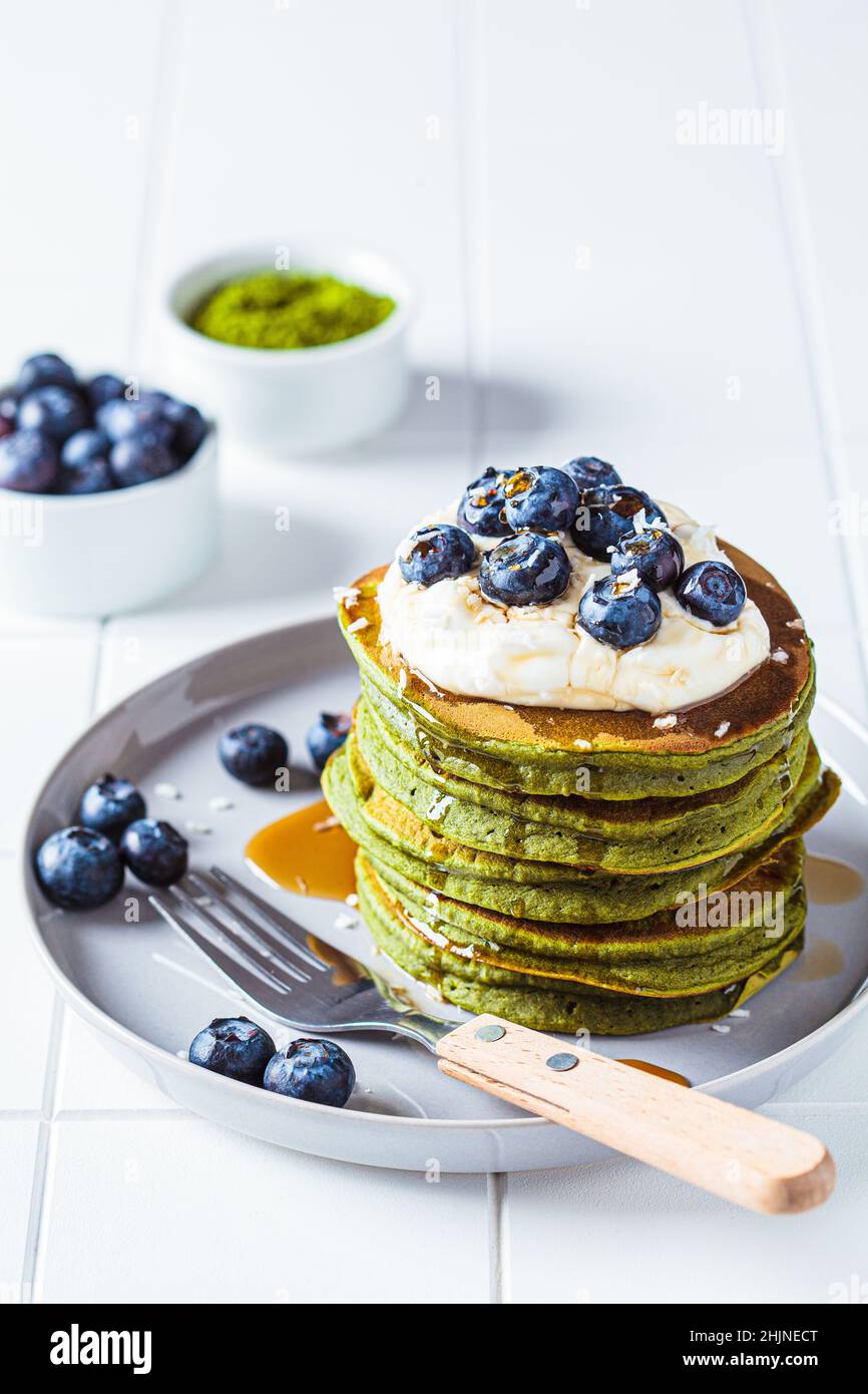 Matcha tea green pancakes with coconut cream, blueberries and maple syrup, white background. Vegan dessert concept. Stock Photo