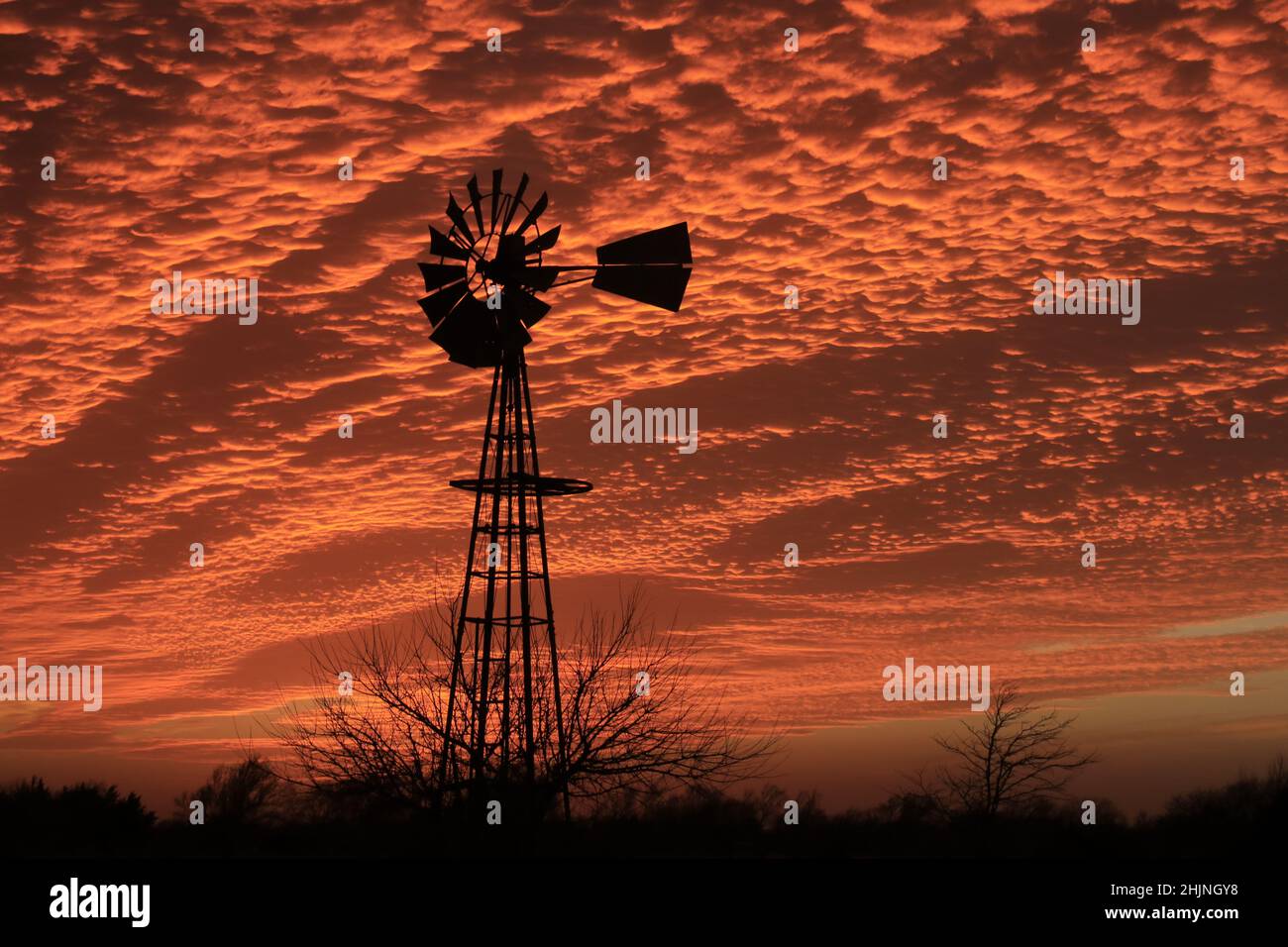 A Kansas colorful Red sky at Sunset with a Windmill silhouette out in the country in a pasture Stock Photo