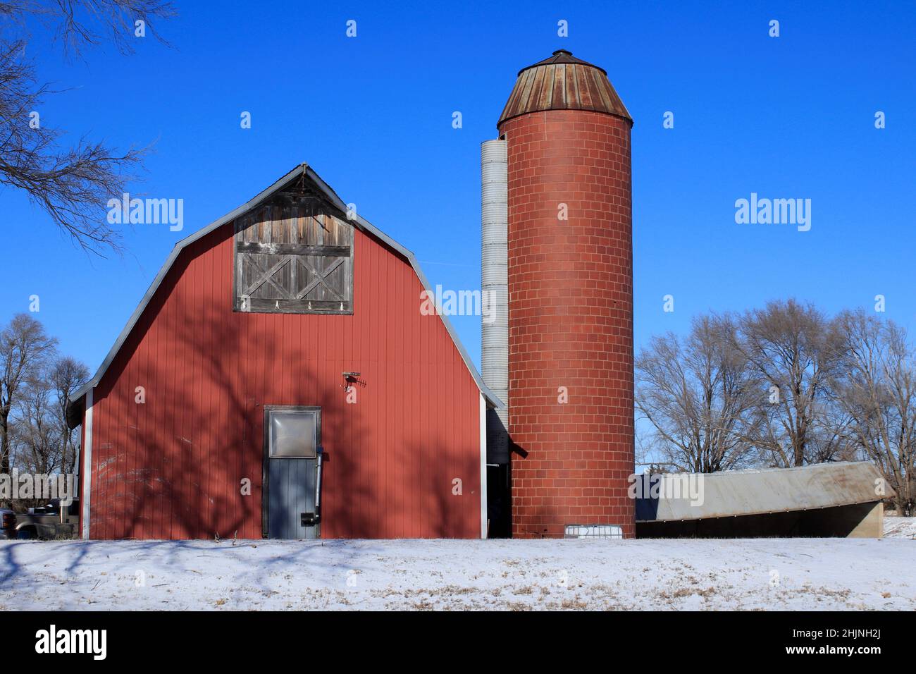 A Red Barn and Silo with snow in the winter time with blue sky in Kansas Stock Photo