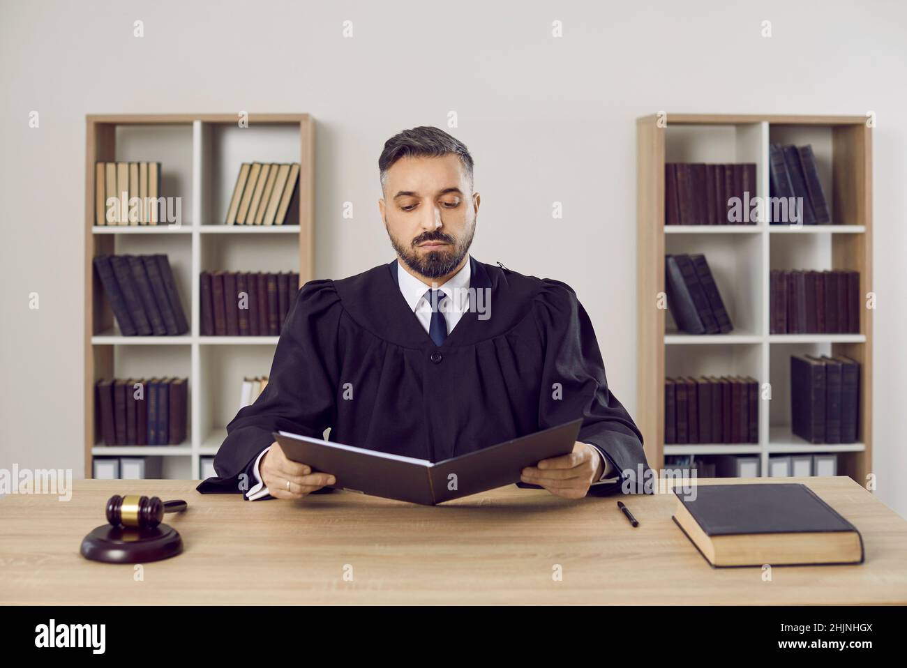 Serious male judge reads legal documents on case sitting at table in his office. Stock Photo