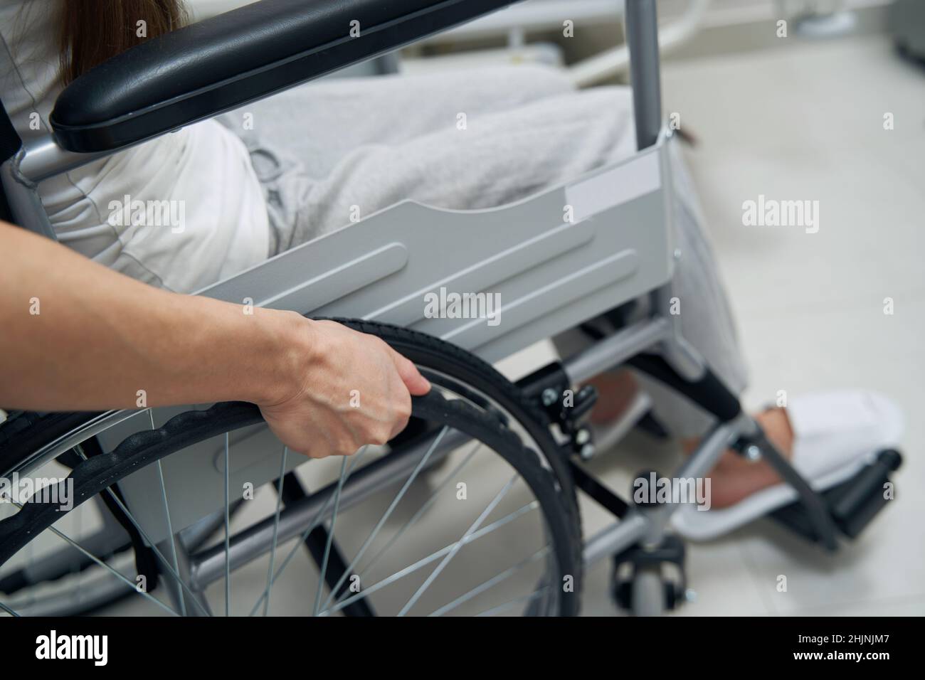 Person with disability propelling wheeled chair in hospital ward Stock Photo