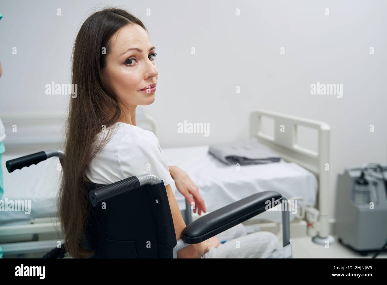 Depressed woman with disability sitting beside bed in hospital ward Stock Photo