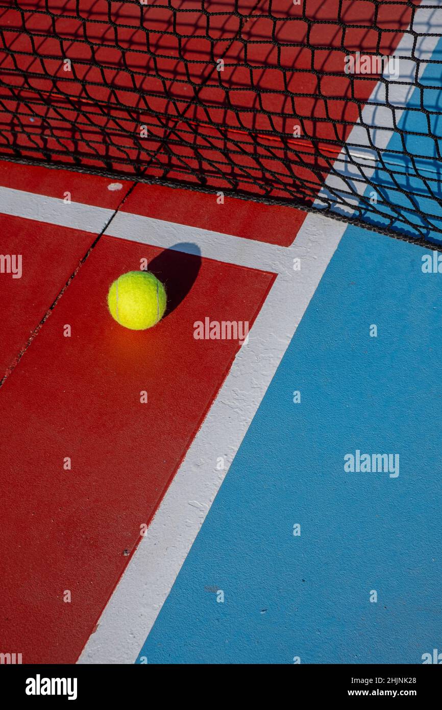 Tennis ball next to the net of a red and blue hard surface tennis court. Racket sports concept. Stock Photo