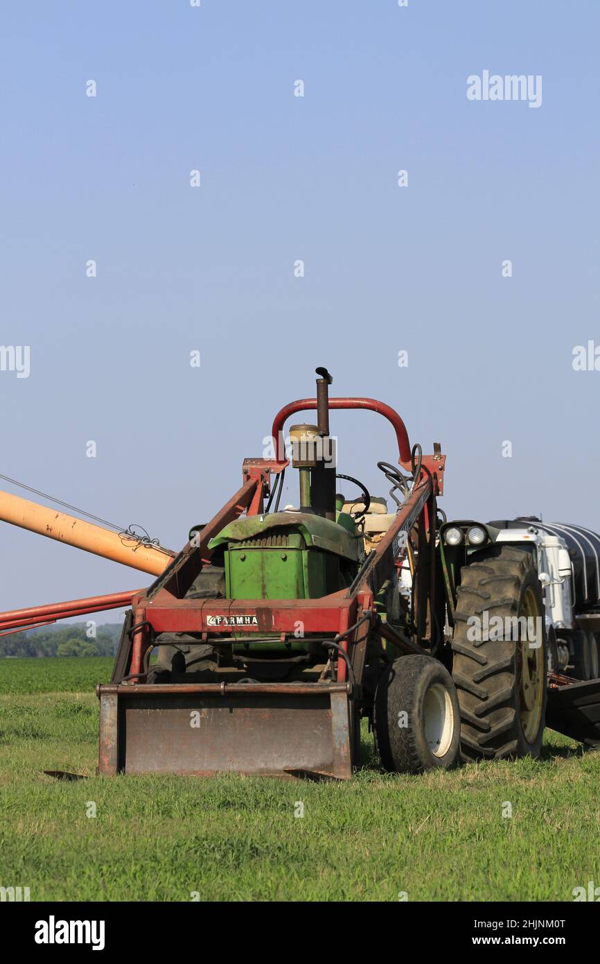 A John Deere tractor with a Farmhand front end loader on it with blue sky out in the country Stock Photo