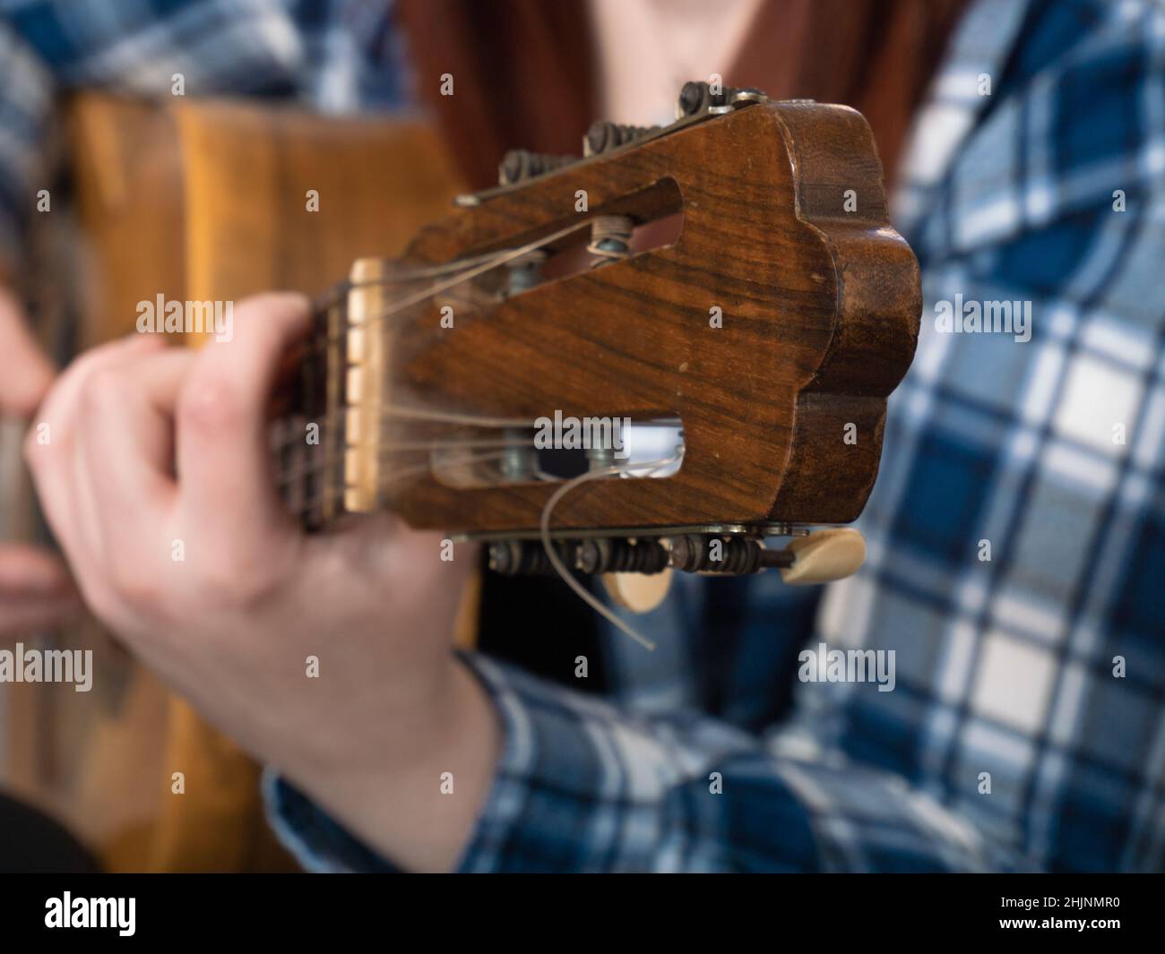 frontal detail view of the neck of an acoustic guitar played by a woman on her sofa at home. Stock Photo