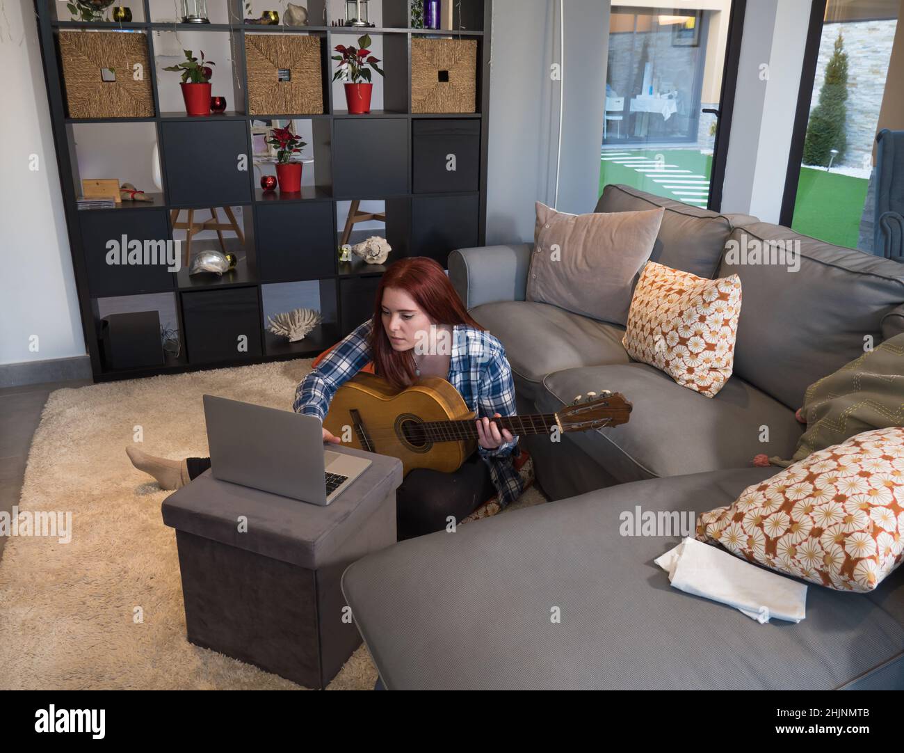 attractive young woman with red hair looking for sheet music on the web while learning to play the guitar in her living room. angular image of the liv Stock Photo