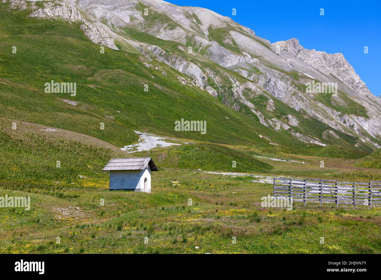 Small chapel on alpine meadow as mountains under blue sky on background at Colle della Maddalena in France. Stock Photo