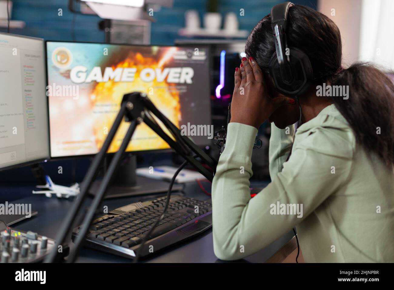 Sad upset pro gamer woman playing space shooter video games losing online championship while talking with players on streaming chat. Nervous streamer using RGB gaming computer. Game over on screen Stock Photo