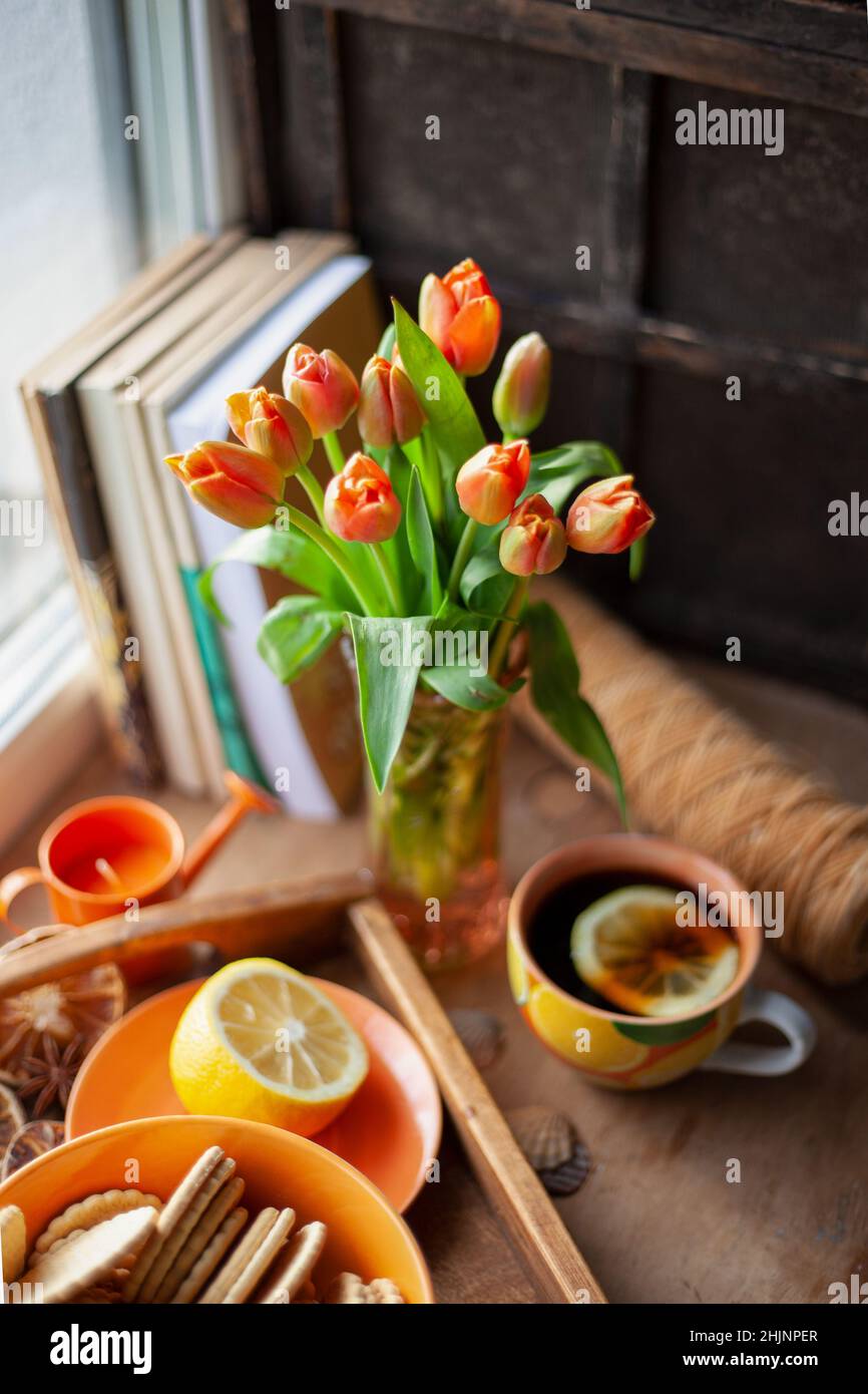 Still life on the table. Bouquet of red tulips and tea with lemon in a cup. Vase. Stock Photo