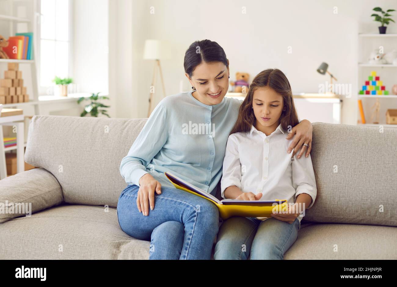 Happy young mother and her child sitting on the couch and reading a book together Stock Photo