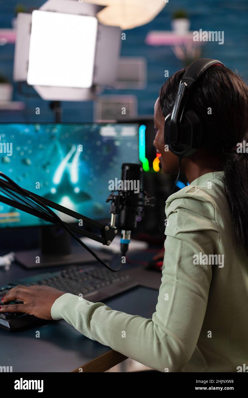 Concentrated pro gamer woman talking into microphone with players using streaming chat while playing space shooter videogames during online championship