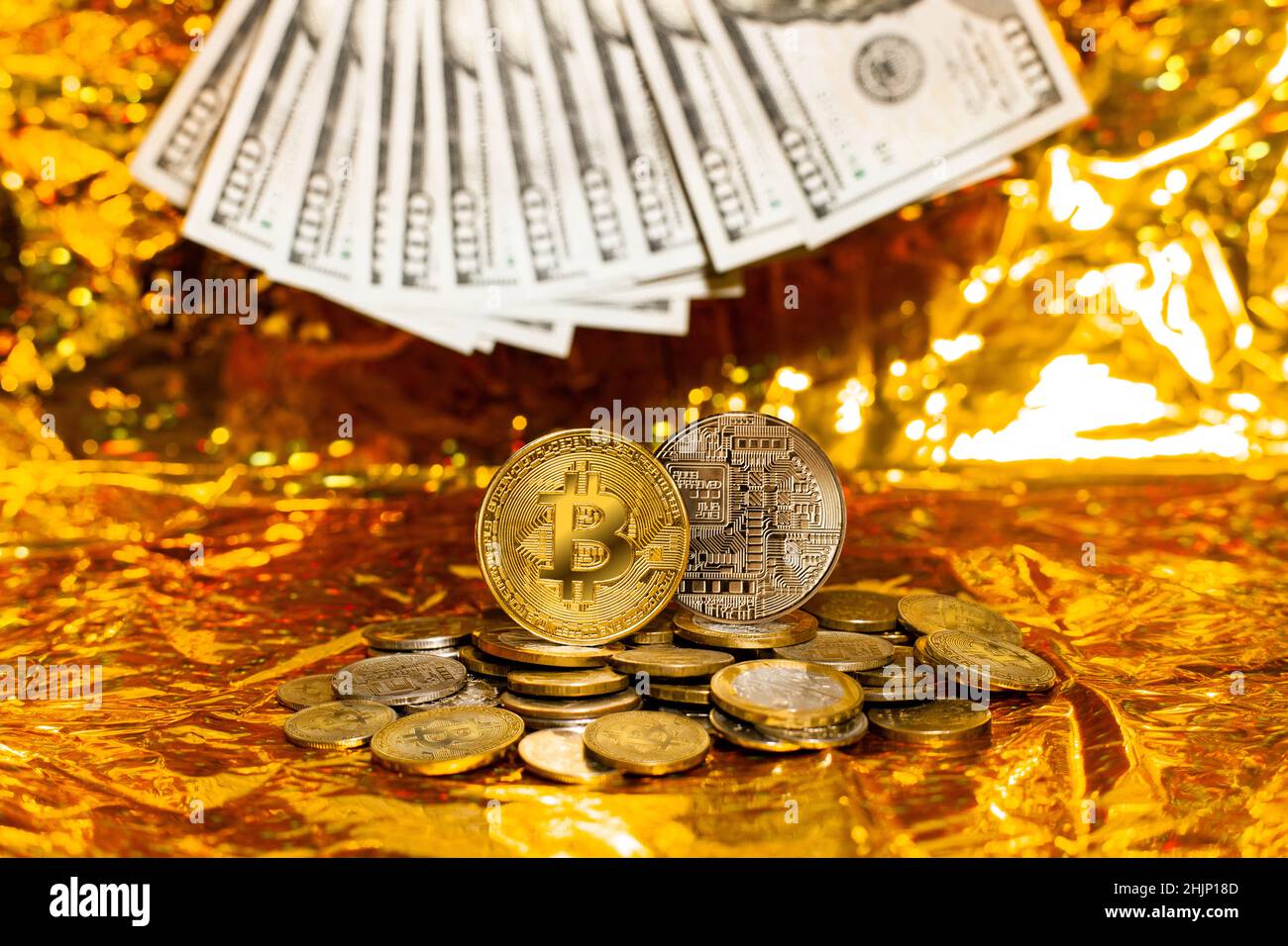 Two bitcoins on a stack of coins against a background of hundred-dollar ...