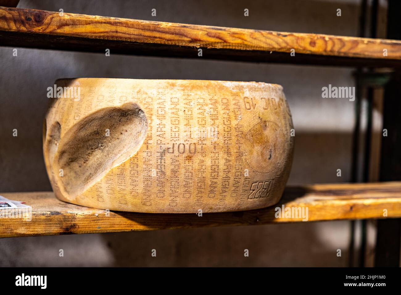 Closeup Of A Damaged Parmesan Cheese Wheel On A Wooden Shelf Of A