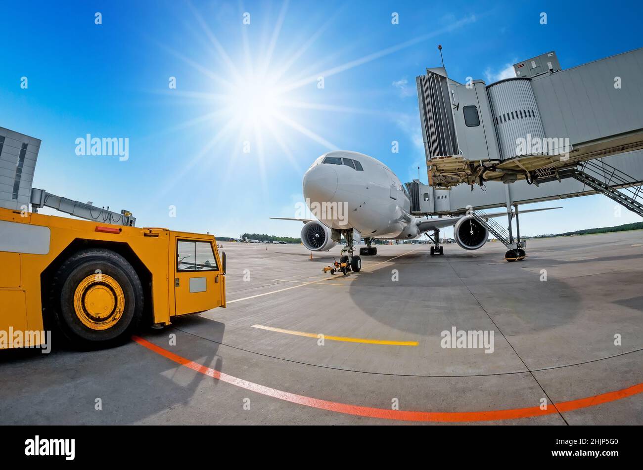 Parking at the airport, airplane at the teletrap. Aerodrome tractor is ready for towing and departure of the aircraft. Against the background of a blu Stock Photo
