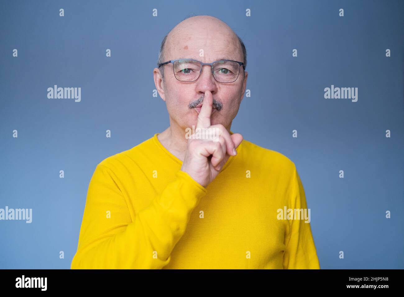Senior hispanic man in glasses making silent gesture isolated over yellow background Stock Photo