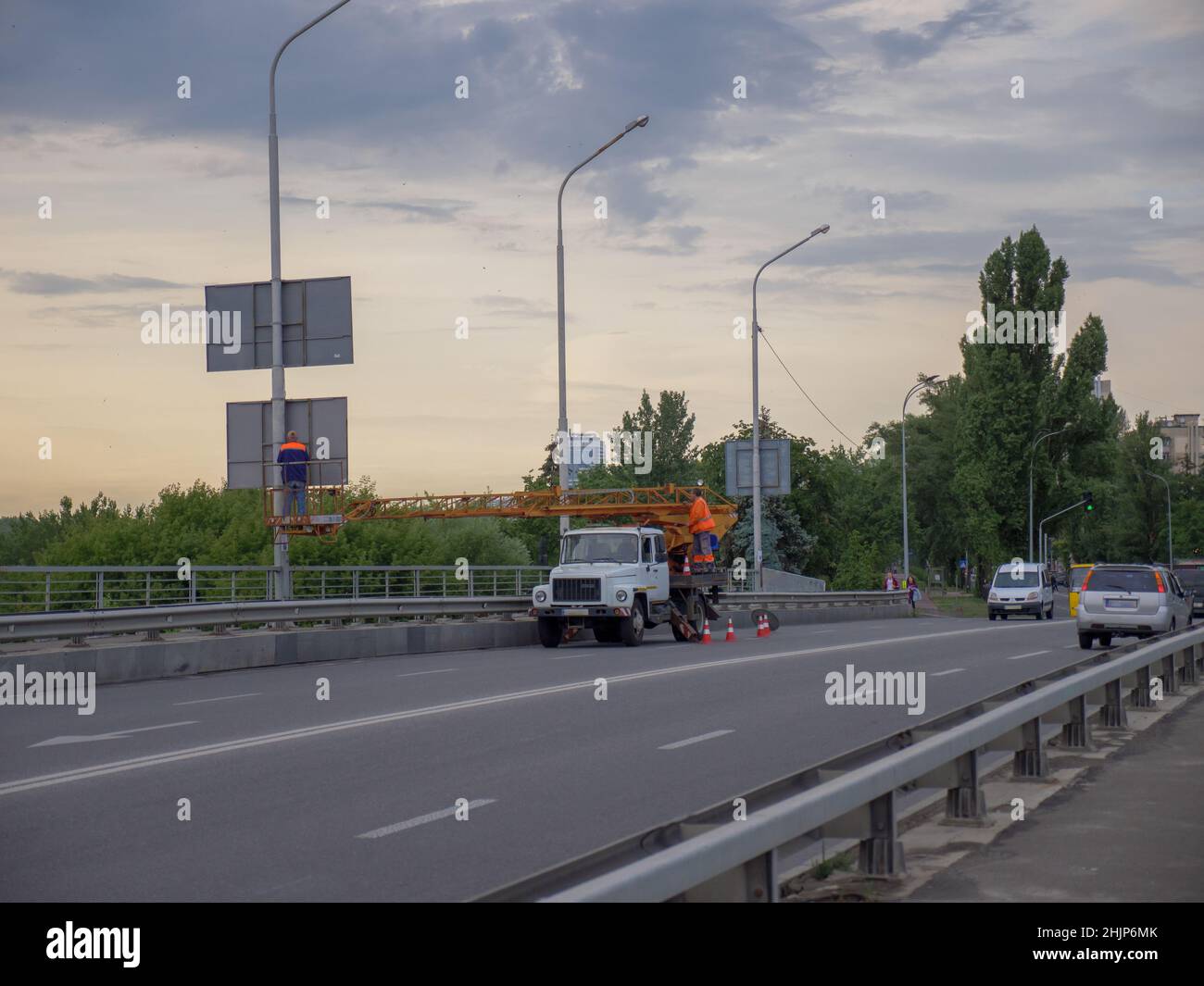 Truck-mounted elevating work platform with two workers doing their job on a road bridge in Kyiv capital city in the evening. Stock Photo