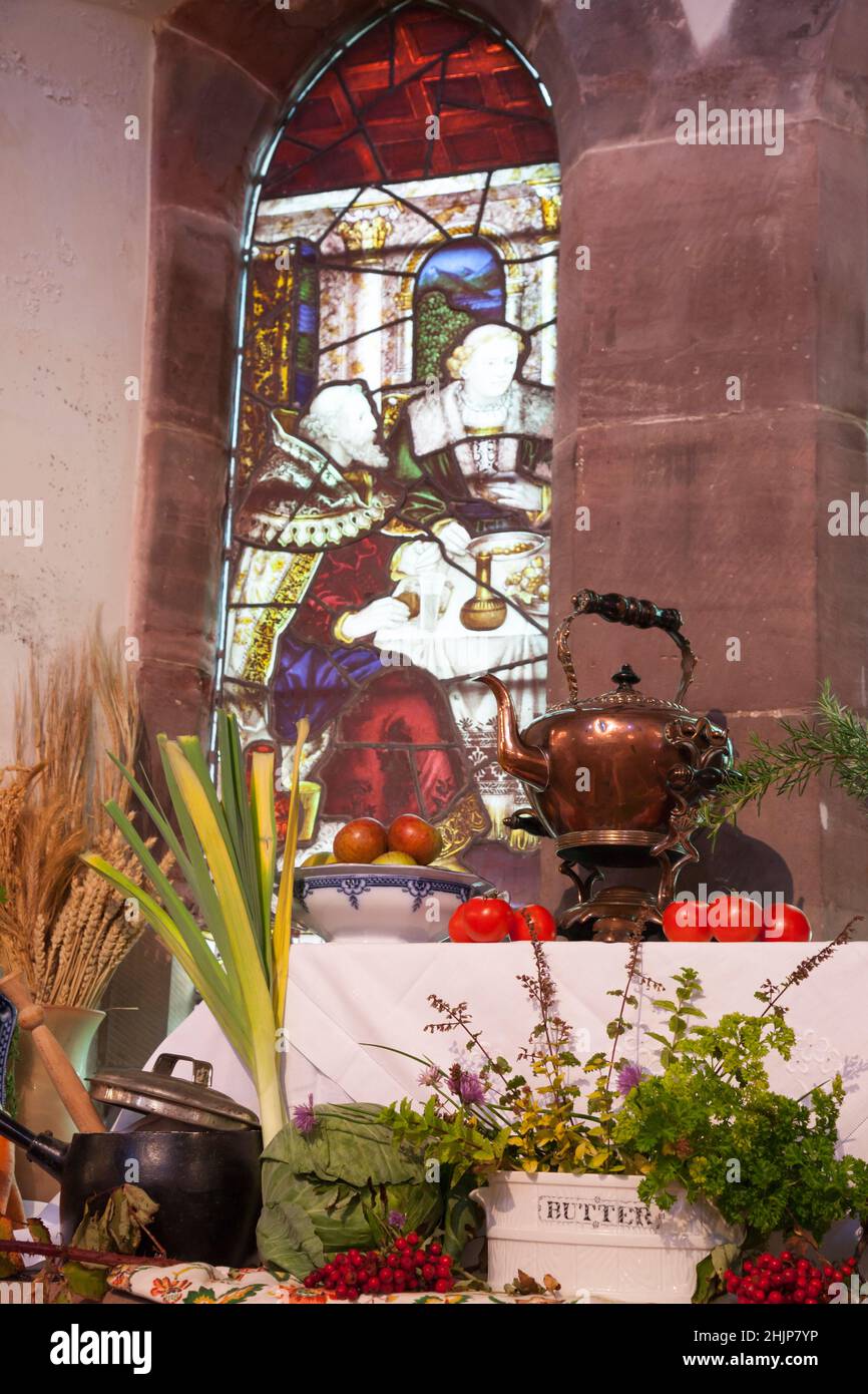 Harvest festival display in St Michael and All Angels Church, Helensburgh, Scotland showing stain glass window and various fruits and vegetables Stock Photo