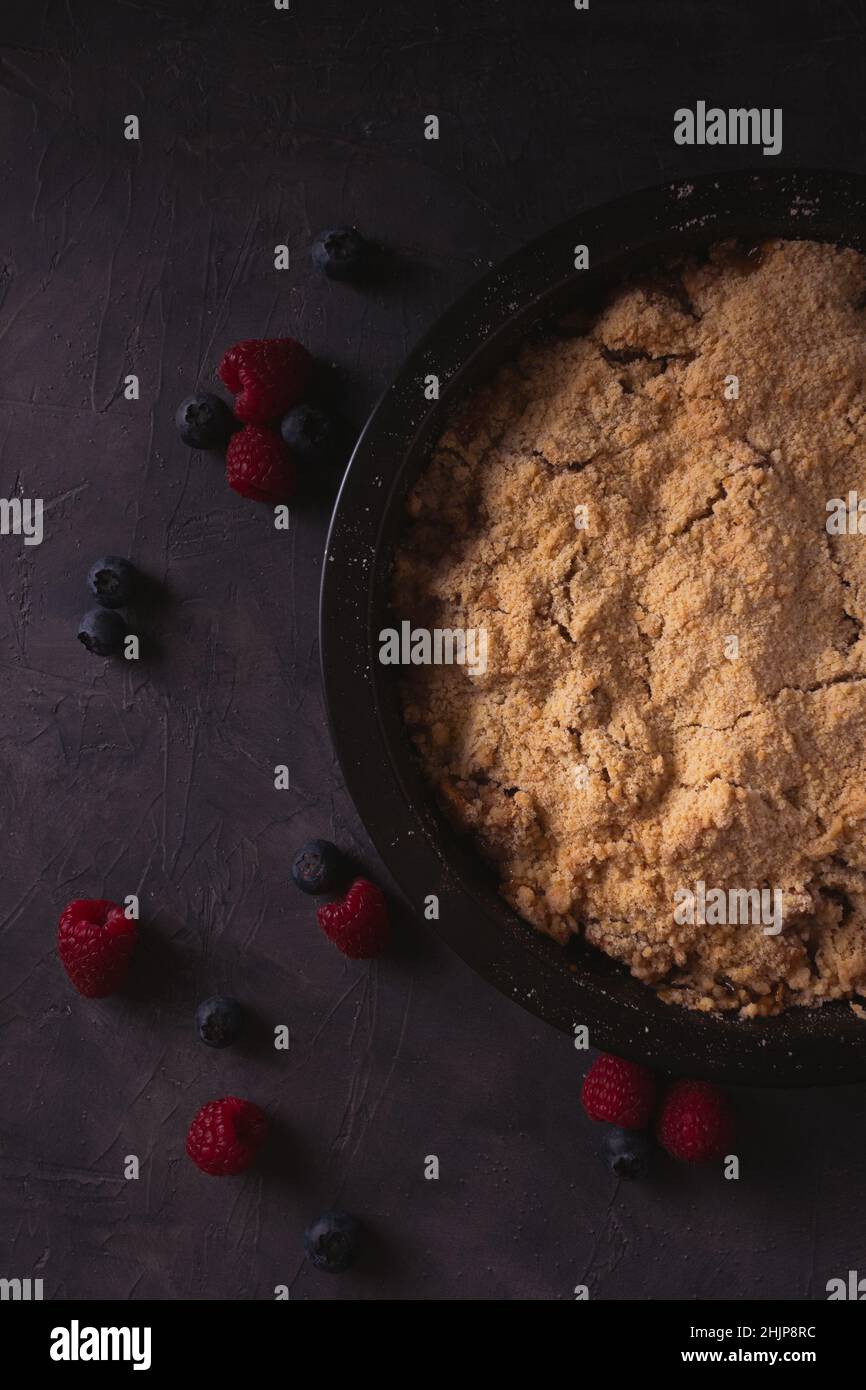 Homemade apple crumble with berries in low light. Dark food photo with copy space. Stock Photo